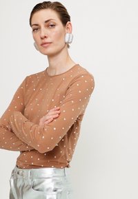 Bluză cu mâneci lungi, de culoare nude, împodobită cu paiete argintii dispersate; asortată cu pantaloni argintii strălucitori, evidențiind o textură fină și o siluetă ajustată.