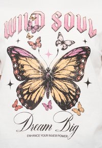 Λευκό μπλουζάκι με μεγάλο γράφημα ενός κίτρινου και μαύρου πεταλούδα με ροζ λεπτομέρειες, περιτριγυρισμένο από μικρότερες πεταλούδες και αστέρια.