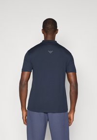 Polo de manga curta azul-marinho com um logótipo discreto nas costas, feito de tecido suave, apresentando um colarinho clássico e linhas limpas.