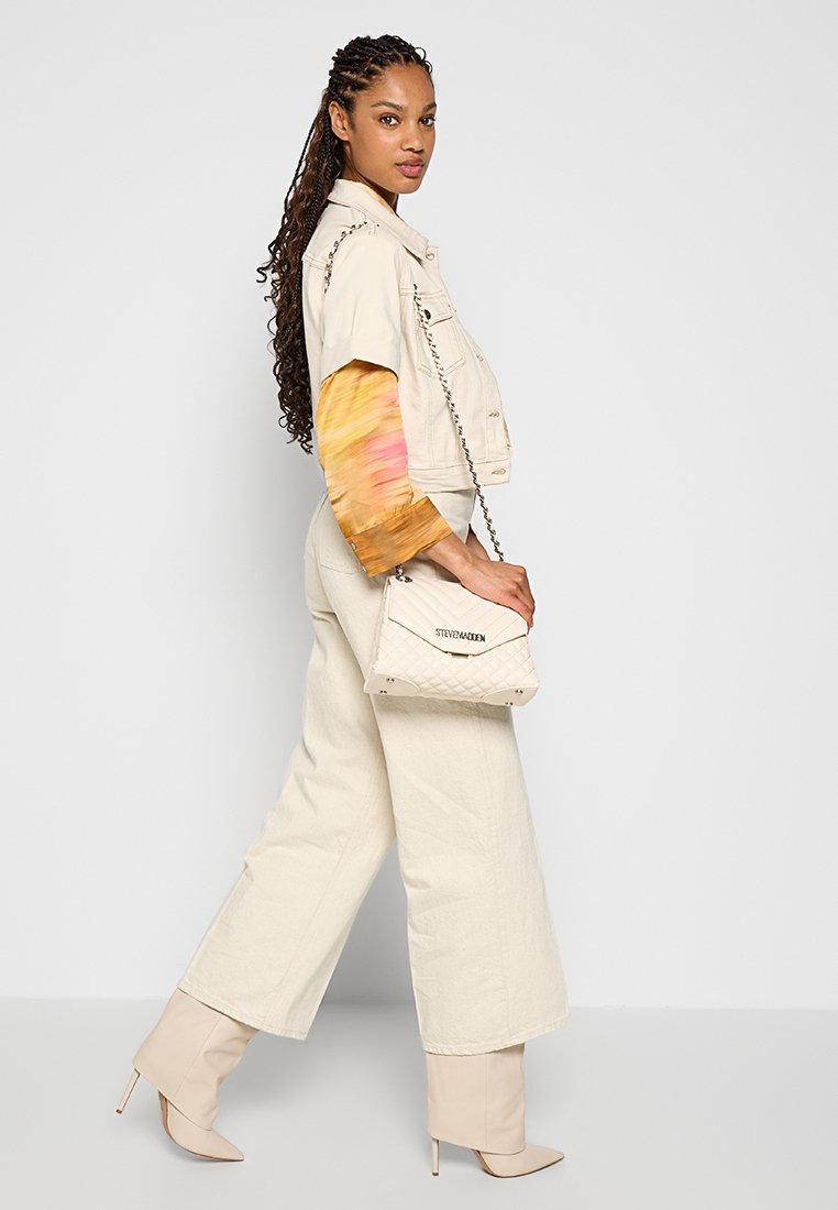Giacca cropped beige con maniche colorate a tinta sfumata, pantaloni beige a gamba larga e una borsa bianca trapuntata. Gli stivali beige alla caviglia completano il look.