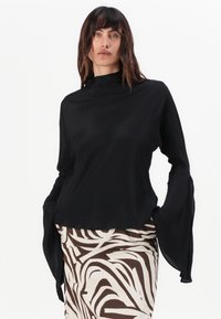 Black long-sleeve top with a high neckline and bell-shaped sleeves, paired with a patterned brown and white skirt featuring an abstract design.