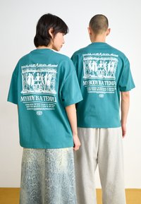Teal cotton t-shirts with graphic designs on the back, featuring white text and patterns, paired with gray sweatpants and snake-print bottoms.