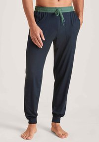 Navyblauwe broek met een groene elastische tailleband, voorzien van zijzakken, taps toelopende boorden en een soepele textuur.