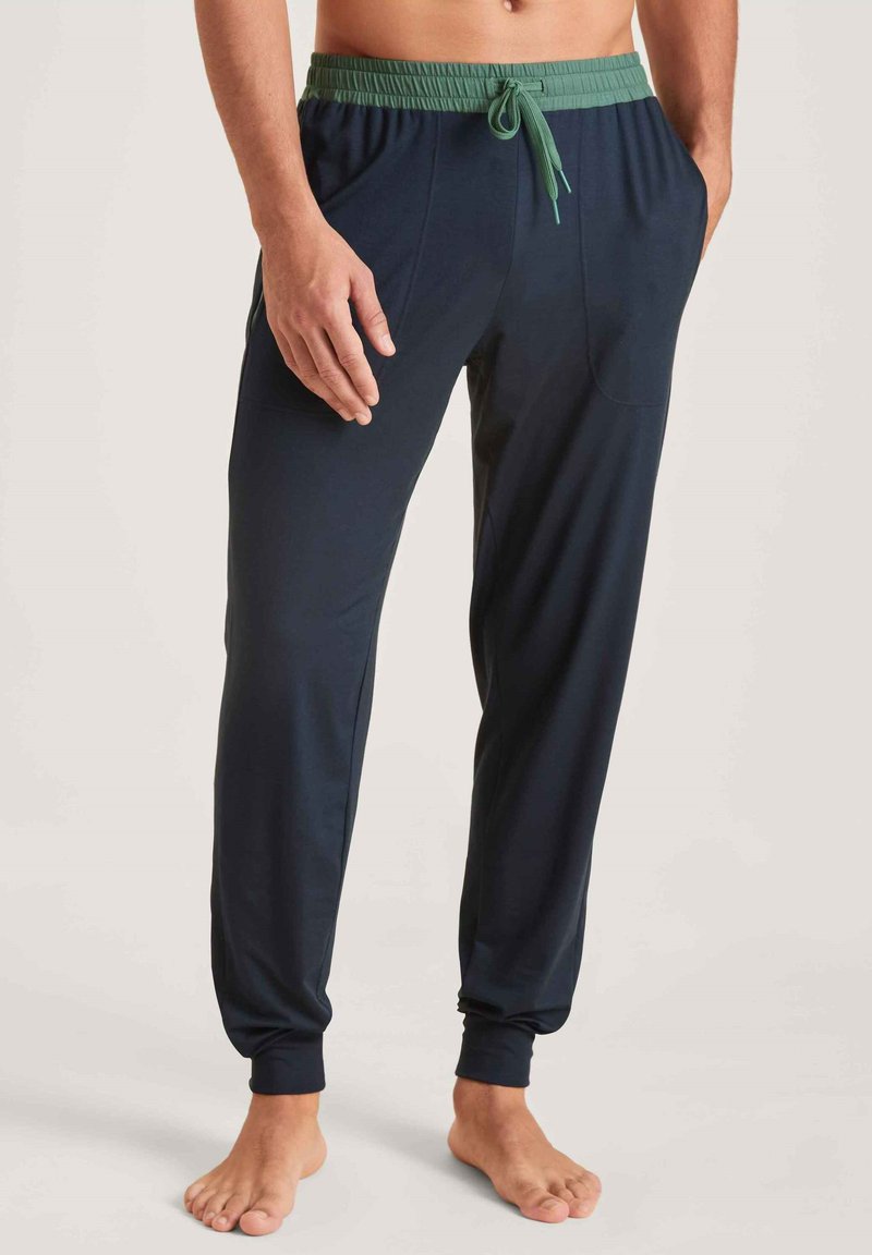 Navyblauwe broek met een groene elastische tailleband, voorzien van zijzakken, taps toelopende boorden en een soepele textuur.