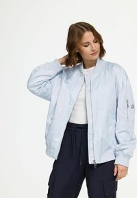 Light blue bomber jacket with a smooth, shiny texture; ribbed cuffs and collar; features zippered pocket on the left arm.