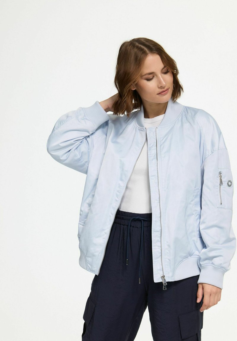 Light blue bomber jacket with a smooth, shiny texture; ribbed cuffs and collar; features zippered pocket on the left arm.