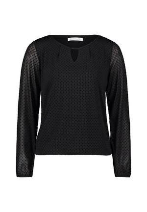 Blouse noire à manches longues en tissu transparent à pois sur les manches et le corps, avec une petite fente en V au niveau du col.