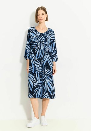 Langarmkleid in Marineblau mit Blauem Blättermuster. Glatter Stoff, lockere Passform, runder Hals und elastischer Bund. Kombiniert mit weißen Sneakers.