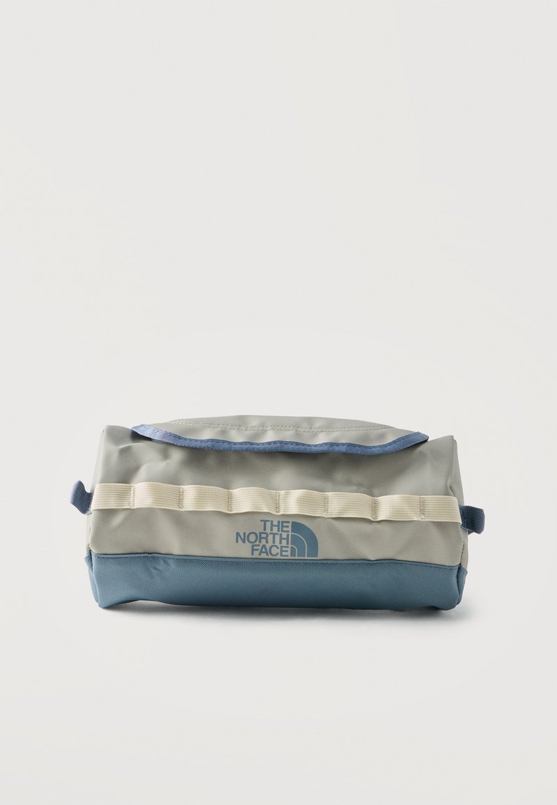 Pochette rectangulaire North Face avec partie supérieure beige, fond bleu, logo sur le devant, fermeture à rabat et passants en sangle beige cousus sur le devant.