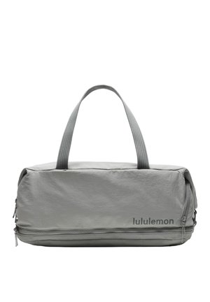 Bolsa tipo duffel Lululemon de color gris claro con asas dobles, bolsillo frontal con cremallera y logo de Lululemon en la parte inferior derecha.