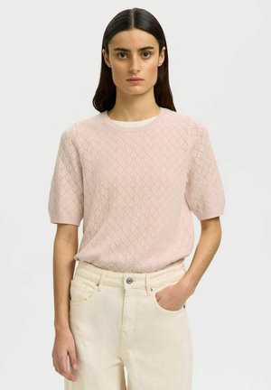 Pulover roz deschis, cu mânecă scurtă, decorat cu un model în formă de diamant și cu guler cu refilet. Asortat cu blugi de talie înaltă, culoare alb-crem.