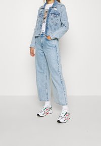 Light blue denim jacket with faded areas, classic collar, and two front pockets. Paired with loose-fitting light blue jeans and colorful sneakers.