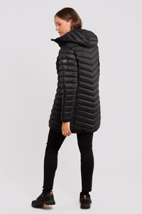 Abrigo acolchado negro con capucha, que presenta un diseño en forma de chevrón y un detalle de logo en el hombro. Se lleva con leggings negros y zapatillas deportivas.