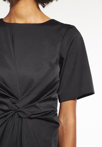 Černé šaty s krátkým rukávem, s detailním zkrouceným uzlem v pase, vyrobené z texturované, lehké tkaniny.