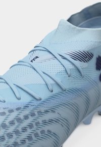 Hellblauer Fußballschuh mit strukturiertem Obermaterial, integrierten Schnürsenkeln und einem sockenähnlichen Knöchelkragen, Nahaufnahme.