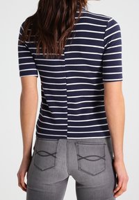 Granatowa i biała w paski bluzka z krótkim rękawem, z detalem szwu z tyłu, w połączeniu z szarymi dżinsami z unikalnymi wzorami na kieszeniach.
