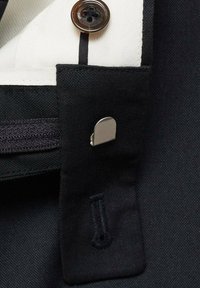 Čierny textil s detailom gombíka a strieborným kovovým akcentom. Má kontrastné biele podšitie a vzor šitia.