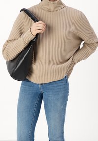 Beige ribbelösa turtleneck tröja med texturerad stickning, ihop med ljusblå skinny jeans. En svart slapp väska hålls i vänster hand.