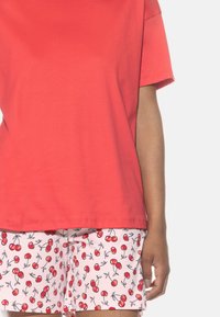 Rotes Baumwoll-T-Shirt kombiniert mit pinken Shorts mit Kirschmuster. Das T-Shirt hat eine lässige Passform; die Shorts zeigen ein florales Design mit grünen Akzenten.