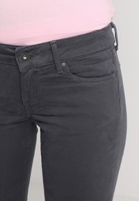 Ciemnoszare dżinsy bawełniane z elastycznym materiałem, o dopasowanym kroju, pięcioma kieszeniami i zapięciem na guzik z przodu. Gładka faktura z dyskretnym przeszyciem.