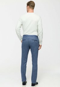 Blauwe textuurbroek met een slim fit, twee achterzakken en een zachte tailleband, gecombineerd met een licht shirt met lange mouwen.