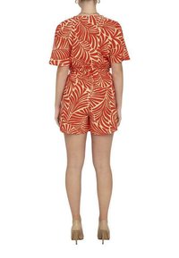 Robe courte à motifs de feuilles tropicaux rouges et beiges, avec des manches courtes et une taille cintrée, associée à des chaussures à talons aiguilles neutres.