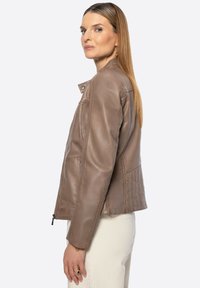 Braune Lederjacke mit tailliertem Design, Stehkragen und Reißverschlussmanschetten. Bietet Seitentaschen und dezente Nähte.