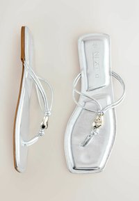 Sandales plates argentées avec fines brides et détail en perles métalliques, design à bout carré, semelles marron et marquage "NEXT" sur la semelle intérieure.