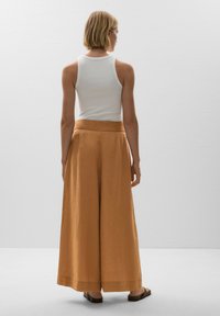 Wide-leg trousers in a warm orange hue, made of lightweight fabric. High waistband and a relaxed fit, paired with a fitted white tank top.