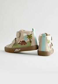 Beige högskor med två kardborreband, prydda med färgglada dinosaurie- och palmträdsdesigner, gummisulor och en ljusblå accent på hälen.