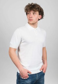 Polo shirt bianco a maniche corte in morbido tessuto a maglia, con colletto classico e polsini a costine, abbinato a jeans in denim blu.