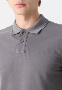 Polo gris en tissu texturé, avec un col, deux boutons et un logo "BOSS" embossé discret sur la poitrine.