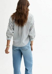 Striped button-up shirt in white and navy, featuring puffed sleeves and a curved hem, paired with light blue straight-leg jeans.