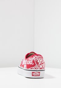 Rote Canvas-Sneaker mit weißen Text- und Logomustern, niedriges Design, weiße Gummisohle und geprägte Fersenlasche.