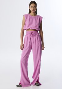 Conjunto de dos piezas que consiste en un crop top rosa sin mangas y pantalones rosas de pierna ancha a juego, con aberturas en el dobladillo y una cintura elástica.