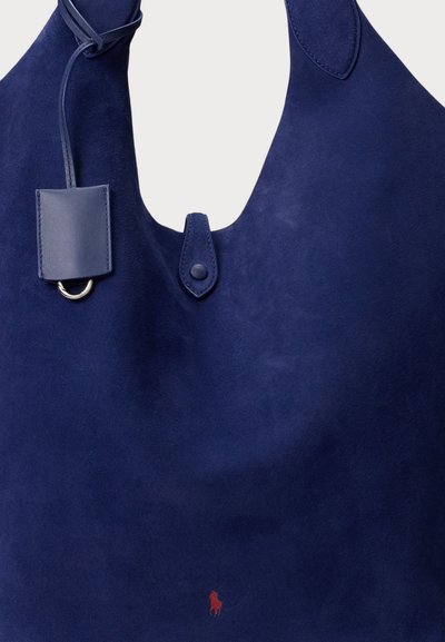 Sacoche en cuir bleu marine avec une texture douce, de forme arrondie, avec une poignée supérieure, une fermeture à pression et un petit logo en rouge.