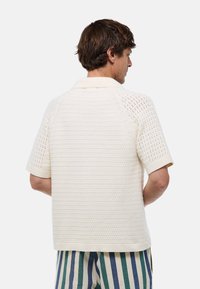 Polo en tricot crème à manches courtes, présentant un motif texturé et un col côtelé. Le dos a un design respirant.