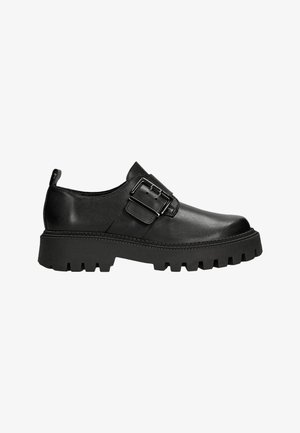 Scarpe in pelle nera con suola spessa, caratterizzate da un risalto di fibbia d'argento e una texture liscia. La suola presenta un design a profonda scanalatura.
