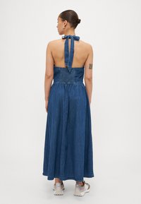 Denim maxi kjole med smocket liv og halterneck-bånd. Har åpen rygg og flytende skjørt. Farge: mørk blå.