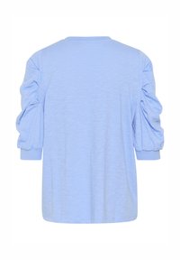 Világoskék, laza fazonú póló puffos ujjakkal és kerek nyakkivágással. Puha tapintású, bordázott mandzsettákkal. A hátoldalon egyszerű dizájn látható.