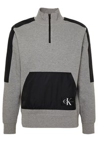 Felpa grigia con zip a un quarto, dettagli in nylon nero sulle spalle e nella tasca frontale, con un patch logo nell'angolo inferiore.
