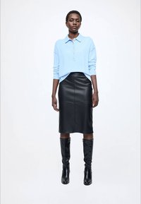 Pulover bleu deschis cu guler și nasturi, asortat cu o fustă midi neagră din piele și cizme negre până la genunchi. Texturi fine, croială ajustată.