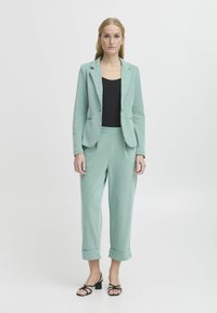 Mintgrön skräddarsydd kavaj och matchande byxor med lös passform, texturerad tyg, uppvikta ärmslut, bärs över en svart topp, svarta remsandaler.