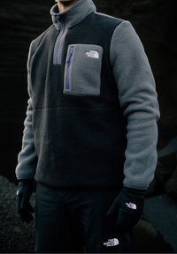 Fleece pullover med halv lynlås i grå og sort. Har en brystlomme med lilla lynlås, lange ærmer og sorte handsker.