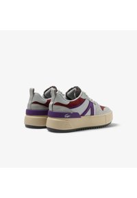 Sneaker grigie e rosse con accenti viola, dotate di un tessuto testurizzato, una suola chunky color crema con battistrada e un logo distintivo sul tallone.
