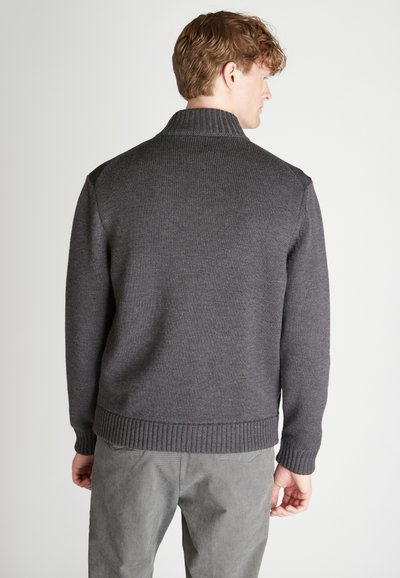 Maglione grigio a maglia con colletto e polsini a coste. Presenta una finitura testurizzata e un design semplice, indossato con pantaloni grigi chiari.