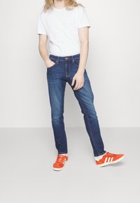 Blå denimjeans med rak passform, bärs med en enkel vit t-shirt och klara orange sneakers. Enkel design, klassisk femficksstil.