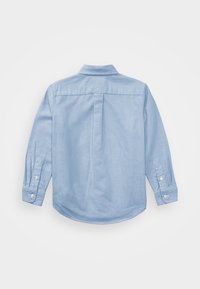 Camisa de manga larga azul claro con cuello, puños abotonados y un pliegue en la parte trasera. Fabricada con una tela suave de textura uniforme.