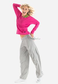 Roze sweatshirt met lange mouwen, gecombineerd met losse grijze trainingsbroek. De broek heeft een drawstring met kleurrijke uiteinden. Witte sportschoenen.