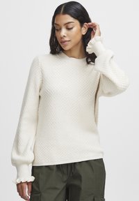 Pull en tricot écru avec un motif texturé, col rond c�ôtelé et manches à volants ; associé à un pantalon cargo olive.
